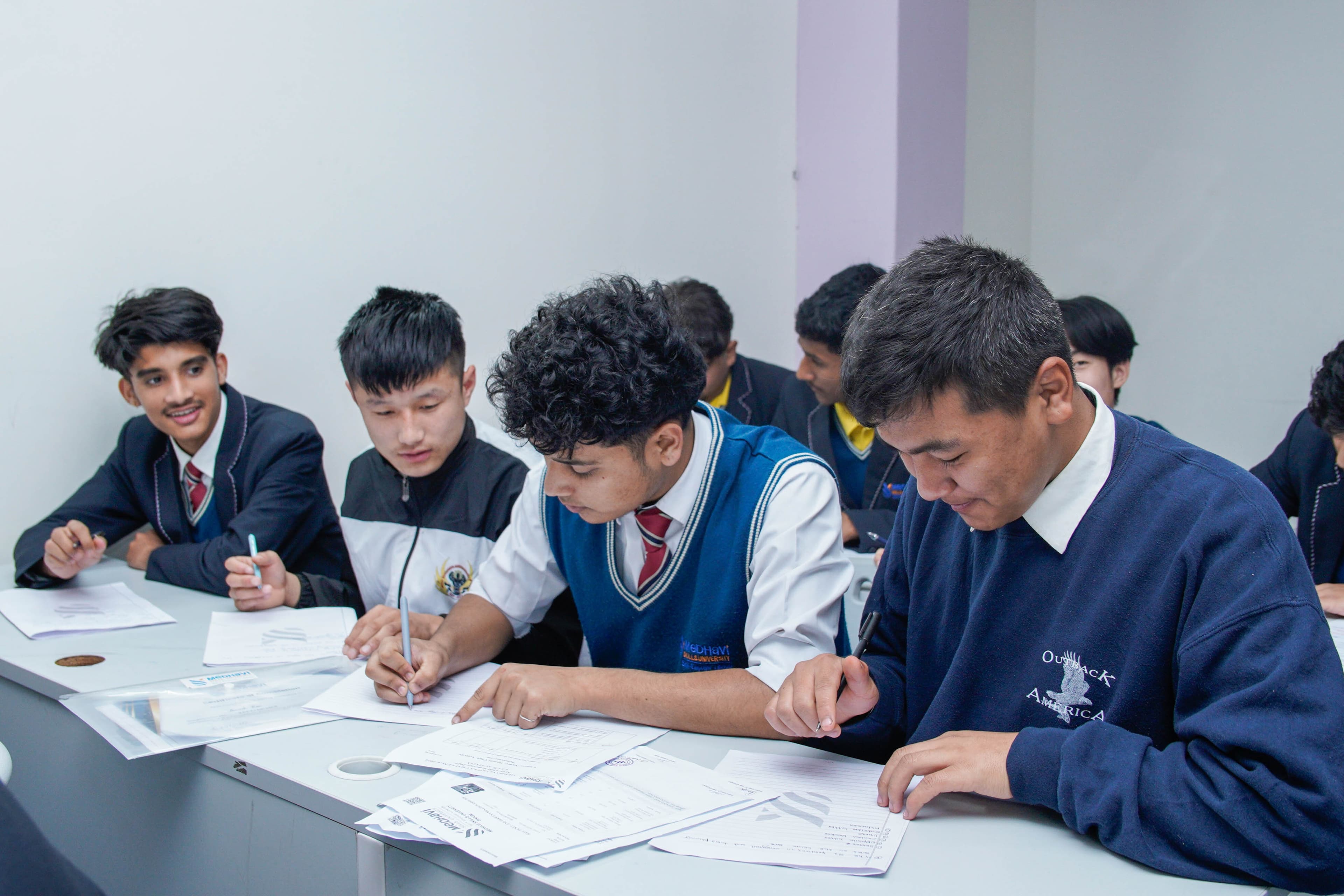 Four graduates in traditional white attire with blue stoles standing together